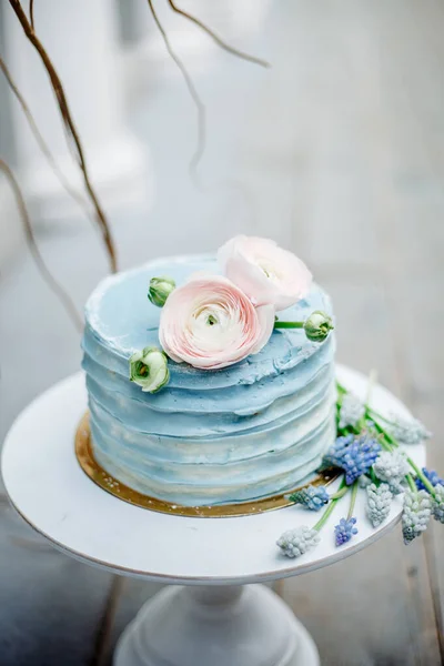 Wedding cake with soft blue cream and decorated with fresh flowers on a white stand.