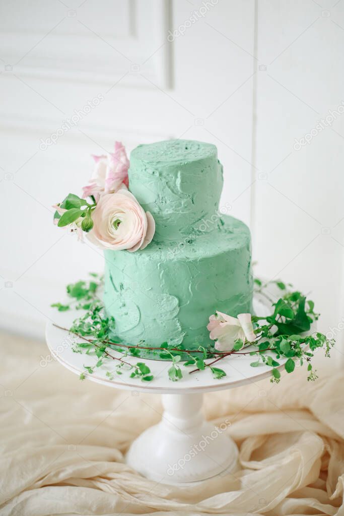 Wedding cake with soft green cream and decorated with fresh flowers in a beautiful interior. Cake in the style of boho