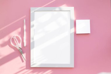 Güneş tarafından aydınlatılan soyut pembe bir masa üzerindeki beyaz bir sayfanın boş bir düzeni. Minimalizm ve modernlik kavramı. Kağıdın altında beyaz kalem, kağıt ve makas..