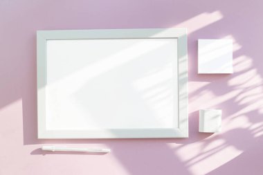 Güneş tarafından aydınlatılan soyut pembe bir masa üzerindeki beyaz bir sayfanın boş bir düzeni. Minimalizm ve modernlik kavramı. Kağıdın altında beyaz kalem ve notlar için kağıt.