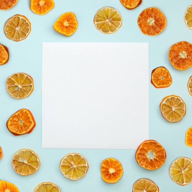 Mavi arka planda kurumuş portakal ve limon dilimleriyle soyut kare arkaplan. Merkezde metin veya resim için beyaz kare bir sayfa var