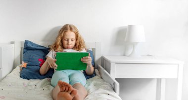 Odadaki küçük bir kızın portresi. Ödevini yapar ya da ped çalar ve yatağa uzanır.