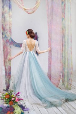 Gelin, ipek bir düğün kemerinde tam boy geriden bir düğün görüntüsüne sahip. Pırıl pırıl mavi gelinlik ve parlak iç mekan.