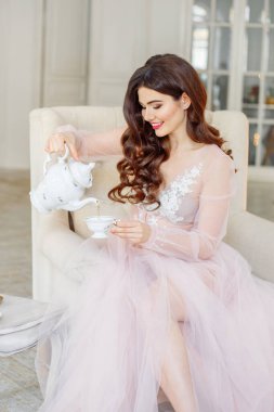 Gelinin sabahı. Beyaz bir iç mekanda çay içiyor. Sandalyeye oturur ve kendine bir fincan çay doldurur.