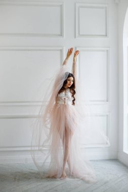 Beyaz iç çamaşırlı, yarı şeffaf elbiseli bir gelinin portresi. O, güzel bir pozla pencerede duruyor.