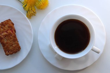 Bir fincan şekerli kahve, kurabiyeler ve sarı karahindiba çiçekleri.