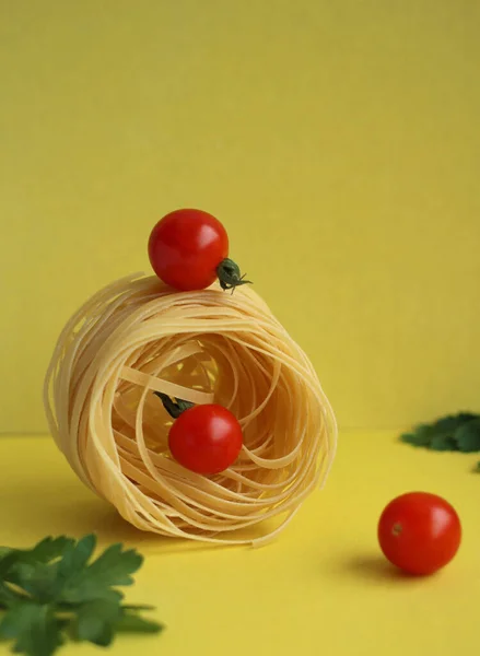 Pasta in the form of a nest with tomatoes and parsley on a yellow background. balance of products — Foto de Stock