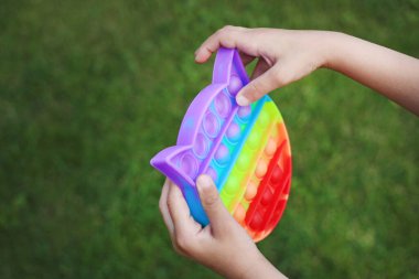 Bir çocuğun elinde, stres önleyici çok renkli bir oyuncak yeşil çimlerin arkasına koyuyor.
