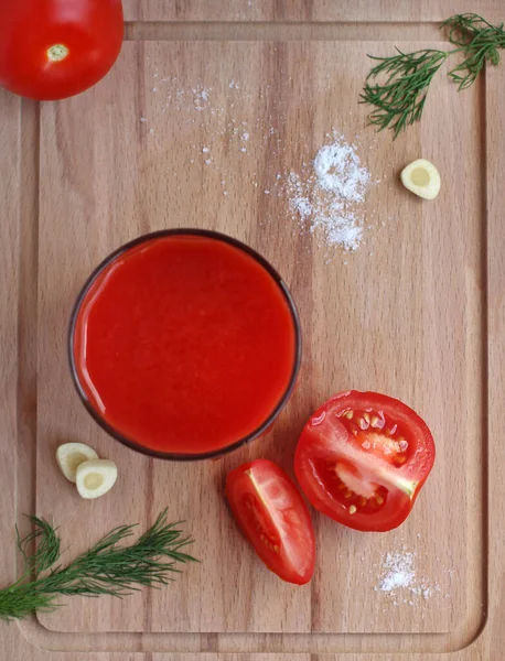 Frischer Tomatensaft im Glas mit Tomaten, Salz, Knoblauch und Kräutern auf einem Holzbrett, Draufsicht — Stockfoto