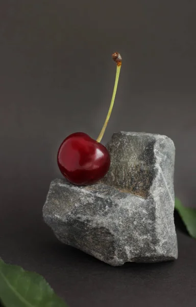 Cherry berries located on a stone in the form of a heart, and cherry leaves on a dark background — Stock Photo, Image