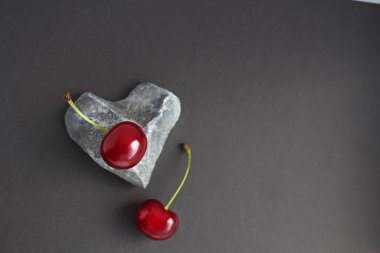 Kalp şeklinde bir taşın üzerine yerleştirilmiş kiraz meyveleri ve koyu arkaplanda kiraz yaprakları.