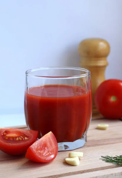 Sumo de tomate fresco num copo com tomate, sal, alho e ervas numa tábua de madeira — Fotografia de Stock