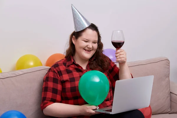 Una giovane donna festeggia il suo compleanno online con un bicchiere di vino in mano. — Foto Stock