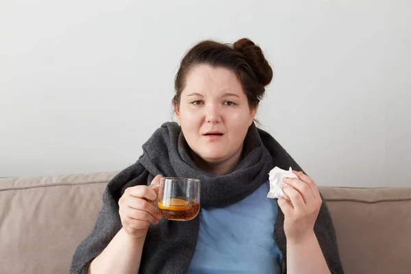 Una mujer joven, está enferma y tomando té caliente. Mira la cámara.. — Foto de Stock