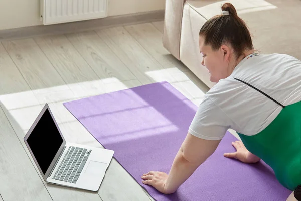 Зайва вага жінки робить йогу вдома в Інтернеті. Поруч з ним відкритий ноутбук . — стокове фото