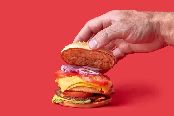 Ik kook een grote Burger. Hand rust een half broodje op een grote Burger. Rode achtergrond. — Stockfoto