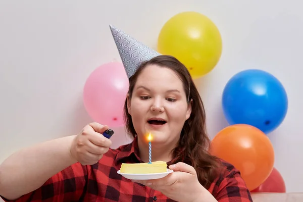 Una joven, una modelo de talla grande, enciende una vela en su pastel de cumpleaños. —  Fotos de Stock