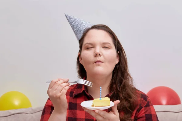 En ung kvinna njuter av en läcker födelsedagstårta med slutna ögon. — Stockfoto