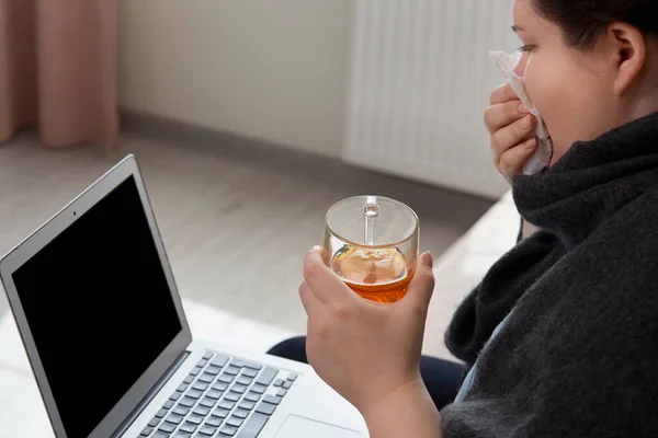 Kobieta jest chora, siedzi w domu na kanapie i patrzy na pusty ekran laptopa. — Zdjęcie stockowe