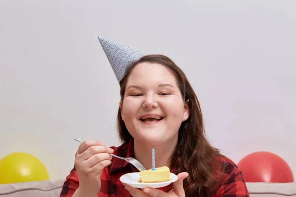 En ung kvinna njuter av en läcker födelsedagstårta och skrattar. Plus storlek modell. — Stockfoto