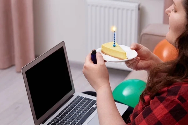 Una giovane donna accende una candela su una torta di compleanno e guarda lo schermo del computer portatile. — Foto Stock
