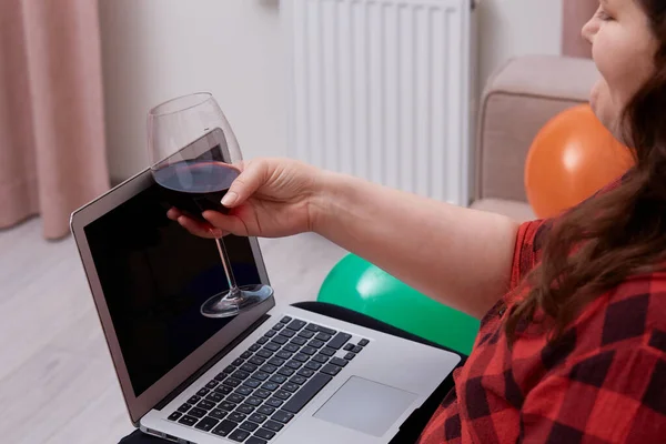 Una mujer sostiene una copa de vino en su mano y mira una pantalla negra en blanco. —  Fotos de Stock