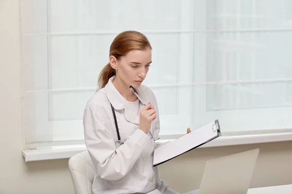 Doctors advice. A young female doctor in a medical gown is holding a clipboard.