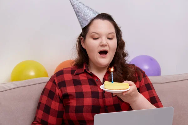 Una joven apaga las velas de un pastel de cumpleaños mientras está sentada en el sofá —  Fotos de Stock