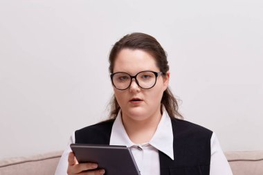 Ofis kıyafetleri içindeki genç bir kadın elinde tabletle kameraya bakıyor..