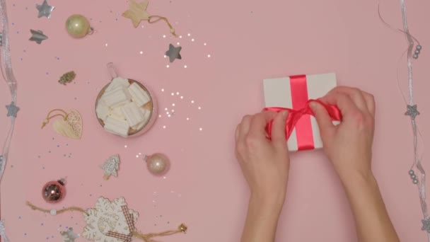 Womens hands tie a red satin ribbon on the box. Flat lay. Pink background. — Stock Video