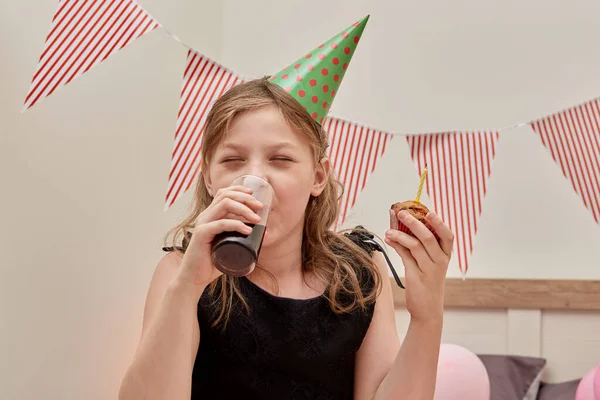 En vacker flicka dricker söt läsk och håller en festlig cupcake i handen. — Stockfoto