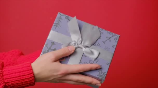 Von oben fällt ein Geschenk in eine Schachtel in der Hand der Mädchen. Zeitlupe. Roter Hintergrund — Stockvideo