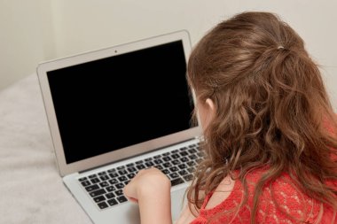 Dalgalı saçlı bir kız bulanık siyah bir laptop ekranına bakıyor. Çevrim içi eğitim.