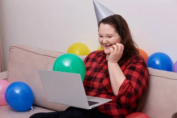 Mujer joven sentada en el sofá riendo y celebrando su cumpleaños en línea. —  Fotos de Stock