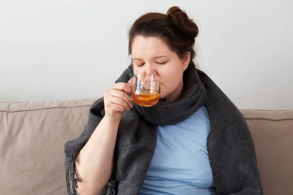 Una donna ha l'influenza, bevendo tè caldo con limone seduto a casa sul divano. — Foto Stock