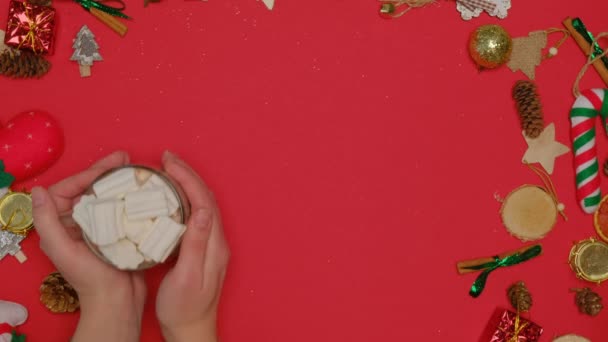 Vrouwen handen zetten een mok warme cacao met marshmallows op een rode achtergrond. — Stockvideo