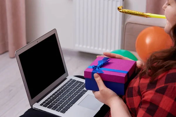Una mujer joven hace sonar un silbato navideño y sostiene una brillante caja de regalo en su mano. —  Fotos de Stock