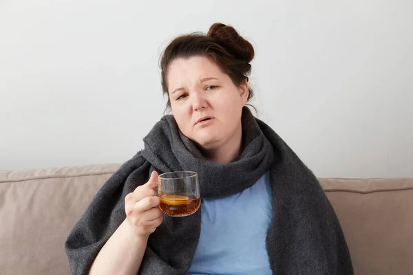 Una giovane donna è malata a casa, con una calda sciarpa grigia intorno al collo. Modello plus size — Foto Stock