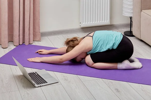 Дівчинка вивчає йогу за допомогою відеозв'язку. Ноутбук на підлозі . — стокове фото