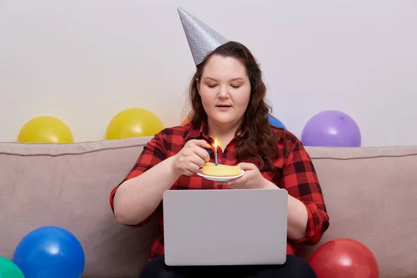 Una joven mujer celebra su cumpleaños en línea con un pastel de cumpleaños en sus manos. —  Fotos de Stock