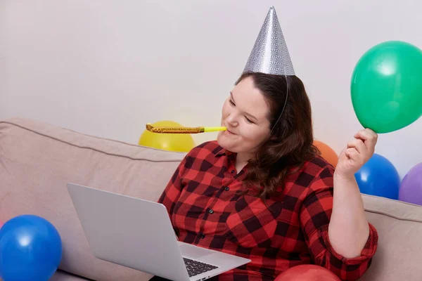 Una joven mujer celebra su cumpleaños en casa en línea. Tocar el silbato navideño. —  Fotos de Stock