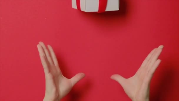Sakta i backarna. En kvinnas händer kastar upp en gåva i en låda. Rött satinband och rosett — Stockvideo