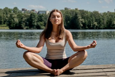 Bir kadın ahşap bir köprüde oturuyor ve yoga yapıyor, gözleri kapalı. Sağlıklı yaşam tarzı.