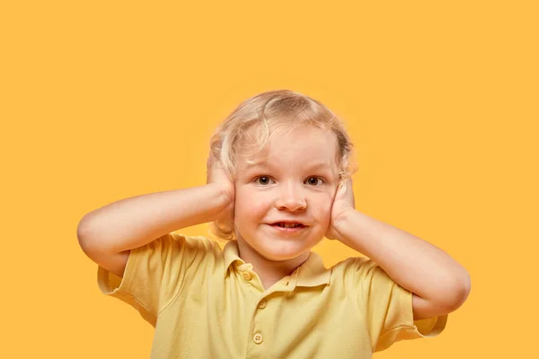 Porträt eines Jungen mit blonden Locken. Deine Ohren sind mit deinen Händen bedeckt. — Stockfoto