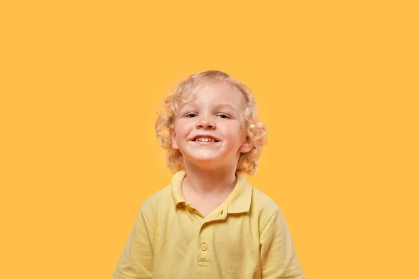Lustige schöne blonde Junge auf einem gelben isolierten Hintergrund schaut in die Kamera. — Stockfoto