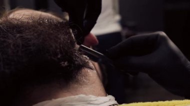 Eldivenli berber tıraş köpüğü ve keskin bir bıçakla sakalını tıraş eder..