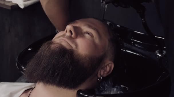 A Barber man washes the head of a bearded customer in a barbershop. — Stock Video