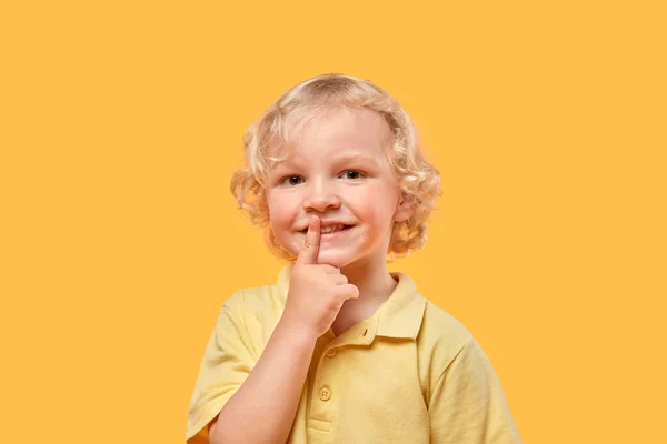 Der Junge mit den lockigen blonden Haaren zeigt eine Tycho-Geste, einen Finger in der Nähe seiner Lippen. — Stockfoto
