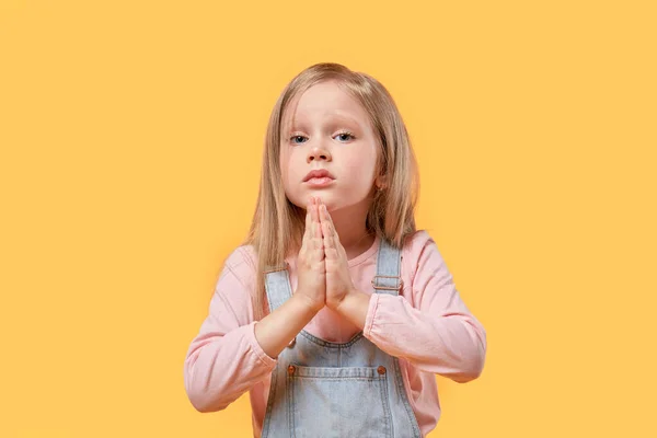 Ein kleines blondes Mädchen blickt in die Kamera und fragt. Handflächen zusammen. — Stockfoto