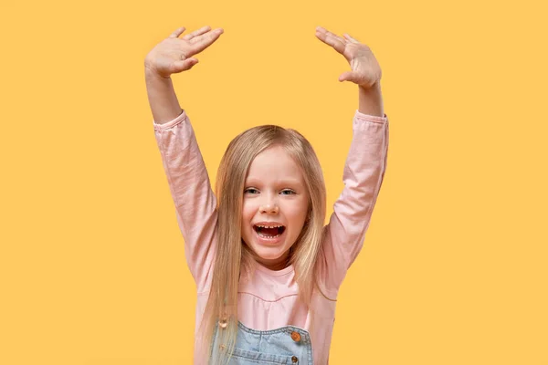 Fröhlich schönes blondes Mädchen hob freudig die Hände. Gelber Hintergrund. — Stockfoto